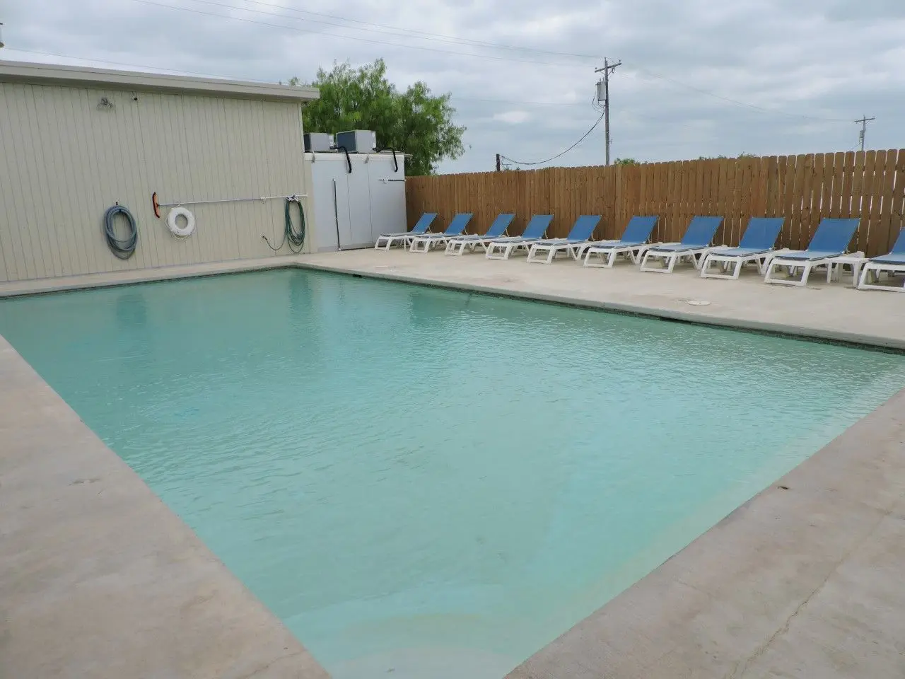 A pool with chairs and a fence in the background.